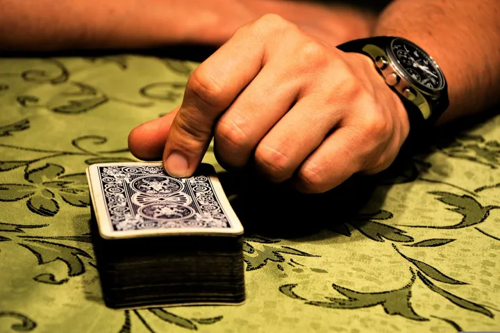 Hand resting on a face-down deck of cards on a patterned green tablecloth